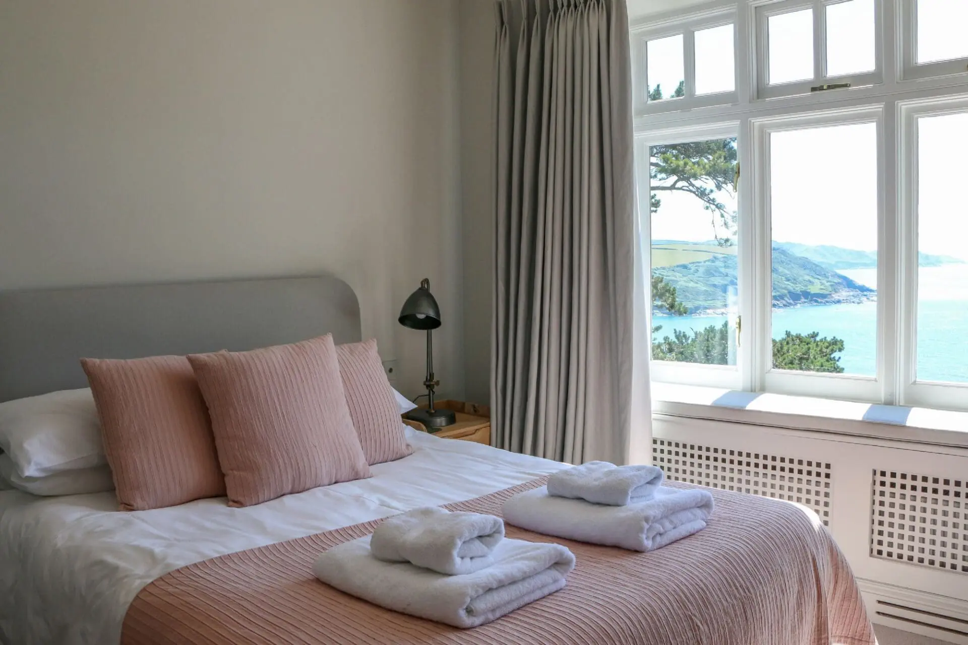 folded towels on bed made with pink linen, sea view out of the window