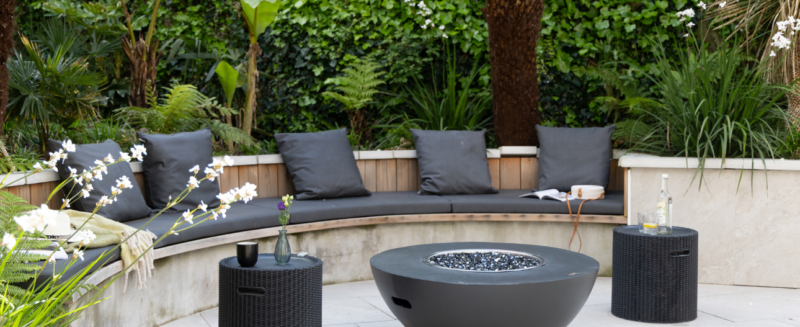 Holiday home garden with curved bench seating and a lit gas firepit