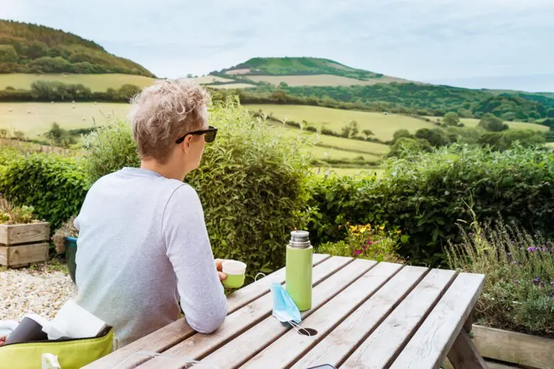 A co-host sitting behind a wooden table and enjoying beautiful local views of Devon.