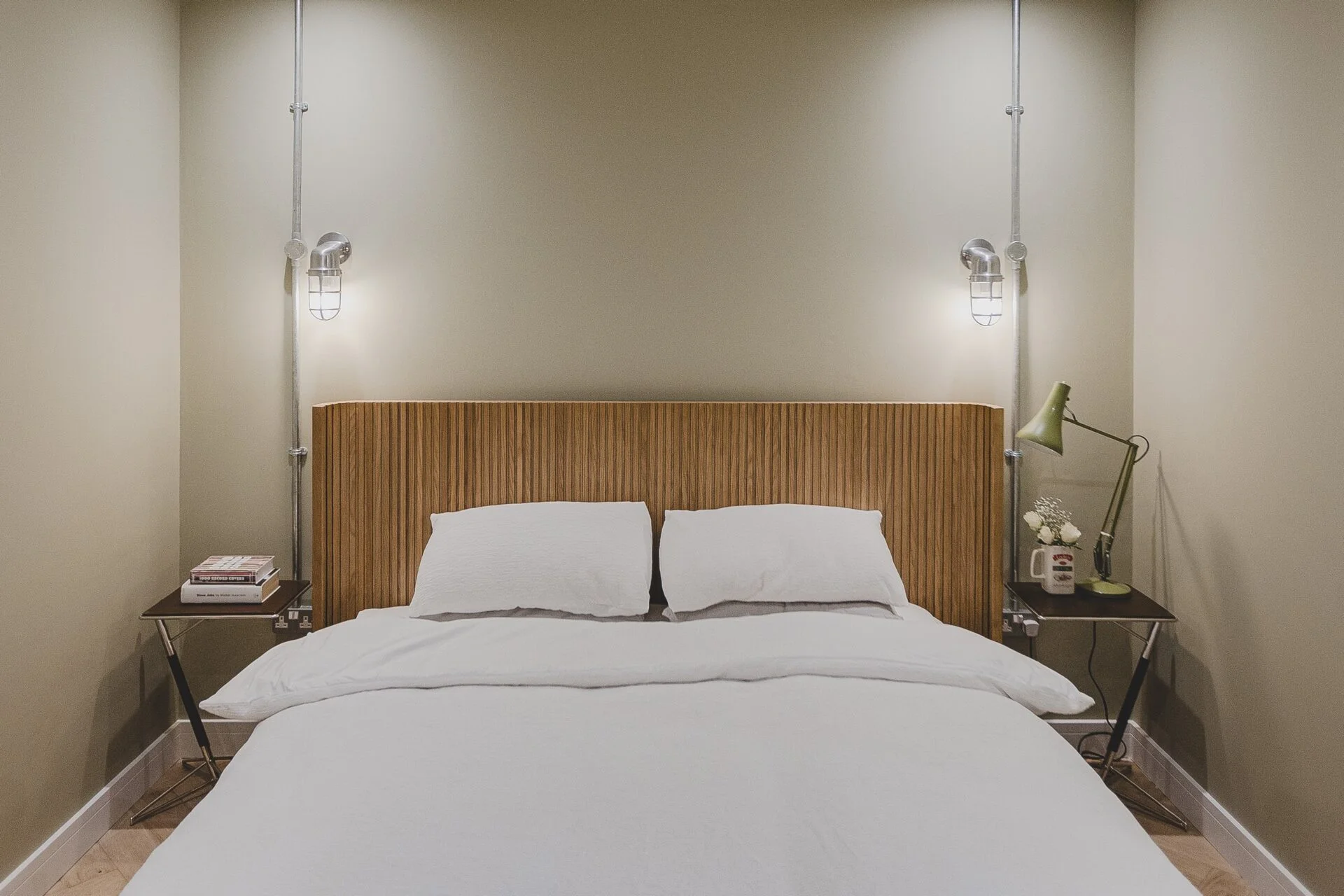 Double bed with a ribbed wooden headboard and brass wall lights at 1 Harlyn Digs