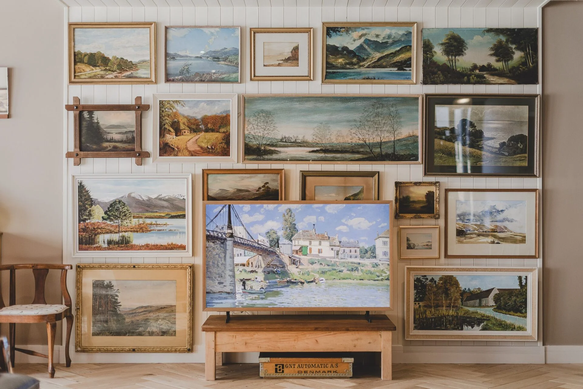 Wall of framed landscape paintings above a low wooden bench at 3 Harlyn Digs