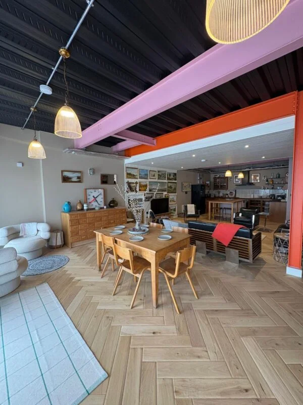 Open plan living and dining space at 3 Harlyn Digs, with herringbone floors and orange steel beams