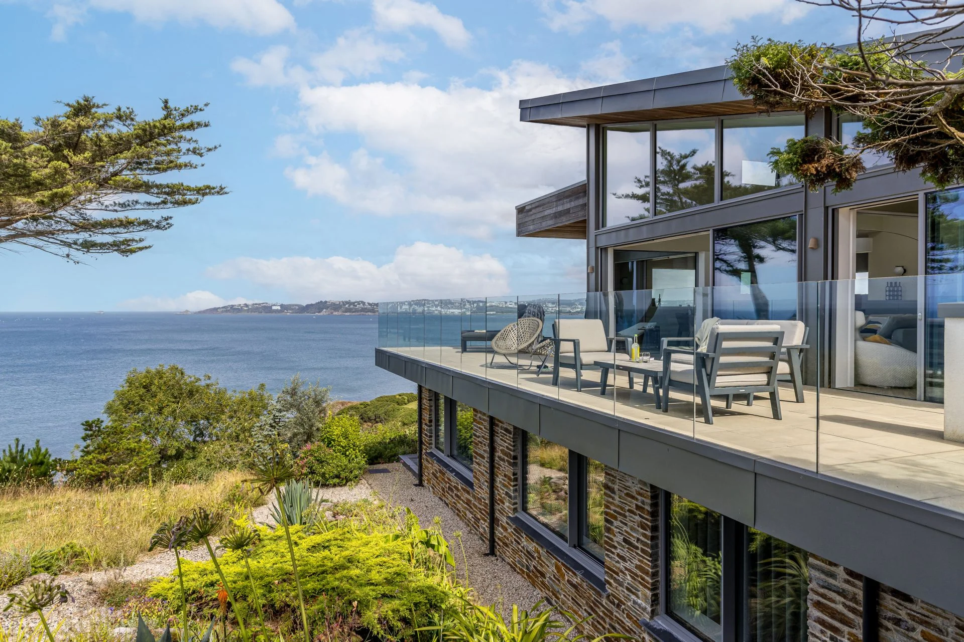 A contemporary clifftop holiday home with a glass-balustraded terrace looking out over the Cornish coast.