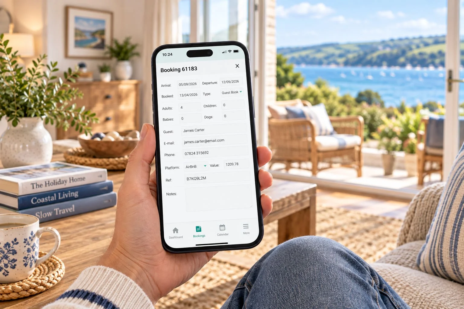 A phone held in a holiday home living room showing guest booking details in the HolidayHost Owner App.